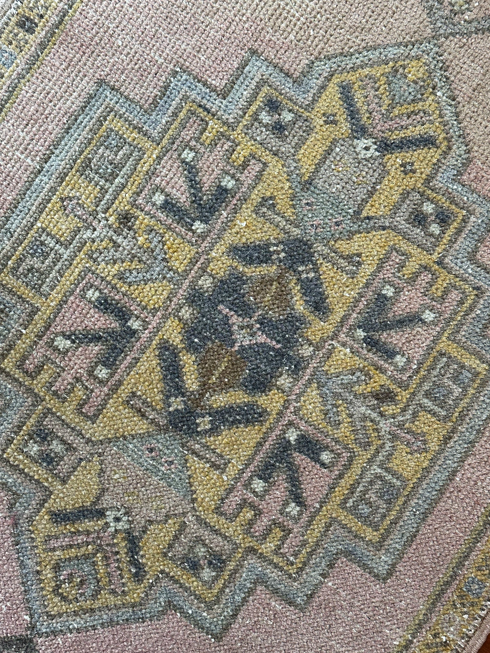 Vintage Turkish wool rug with a central geometric medallion in muted pink, gold, and dark charcoal tones, featuring stepped corner motifs and a distressed finish.
