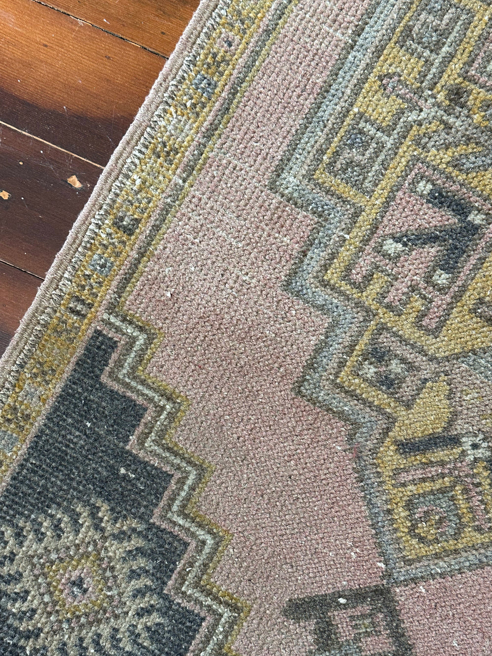 Vintage Turkish wool rug with a central geometric medallion in muted pink, gold, and dark charcoal tones, featuring stepped corner motifs and a distressed finish.