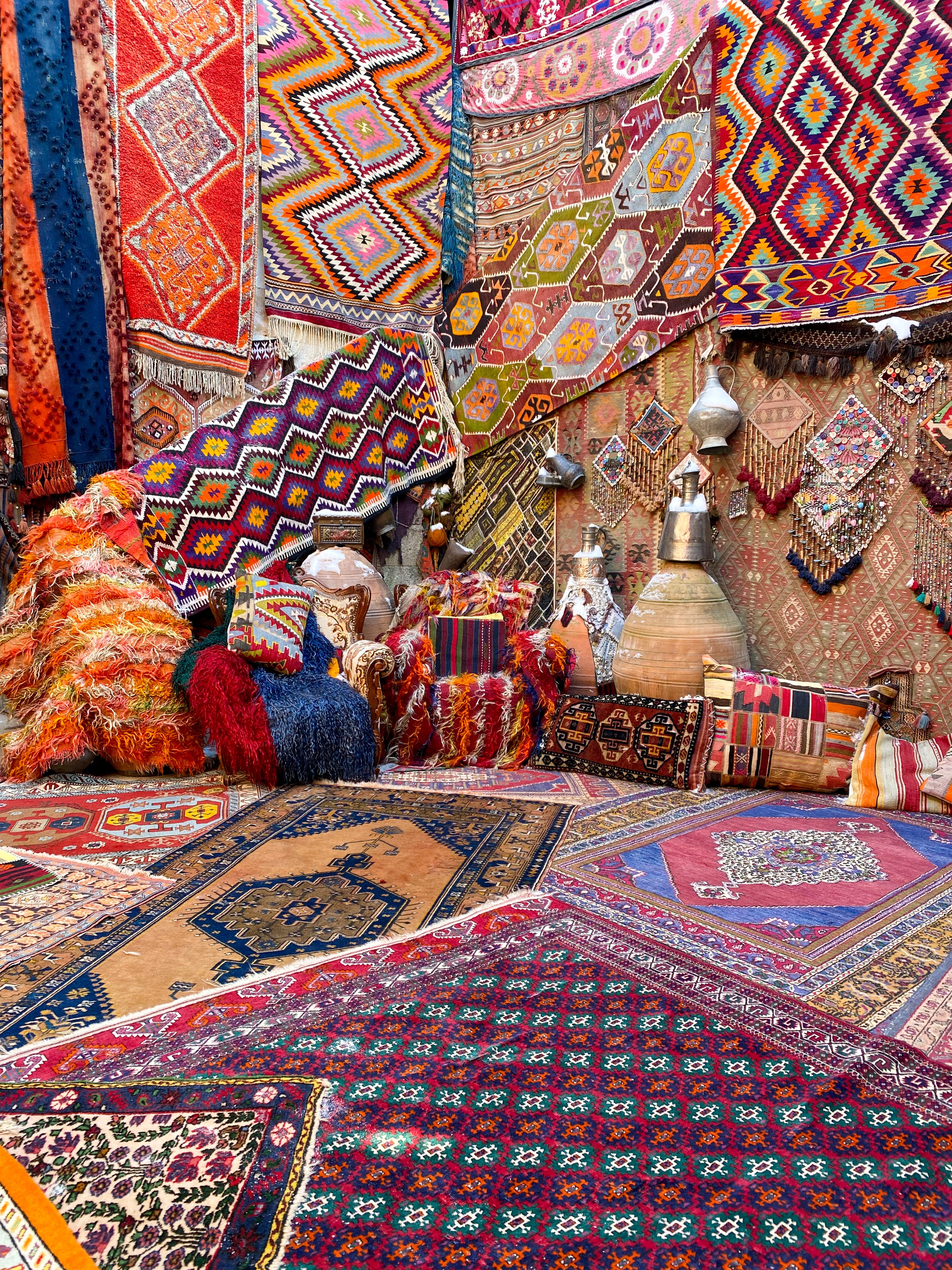 colorful and bright Turkish rugs of different sizes staged together in a showroom. Geometric Turkish pillows surrounding the rugs on the floor.