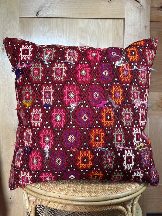 Bold handcrafted kilim pillow with intricate Berber-inspired embroidery. Made from repurposed vintage textiles in deep red, magenta, and orange hues with textured fringe details.