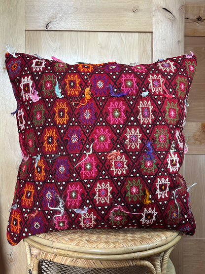 Bold handcrafted kilim pillow with intricate Berber-inspired embroidery. Made from repurposed vintage textiles in deep red, magenta, and orange hues with textured fringe details.