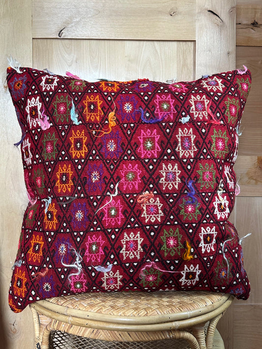 Bold handcrafted kilim pillow with intricate Berber-inspired embroidery. Made from repurposed vintage textiles in deep red, magenta, and orange hues with textured fringe details.