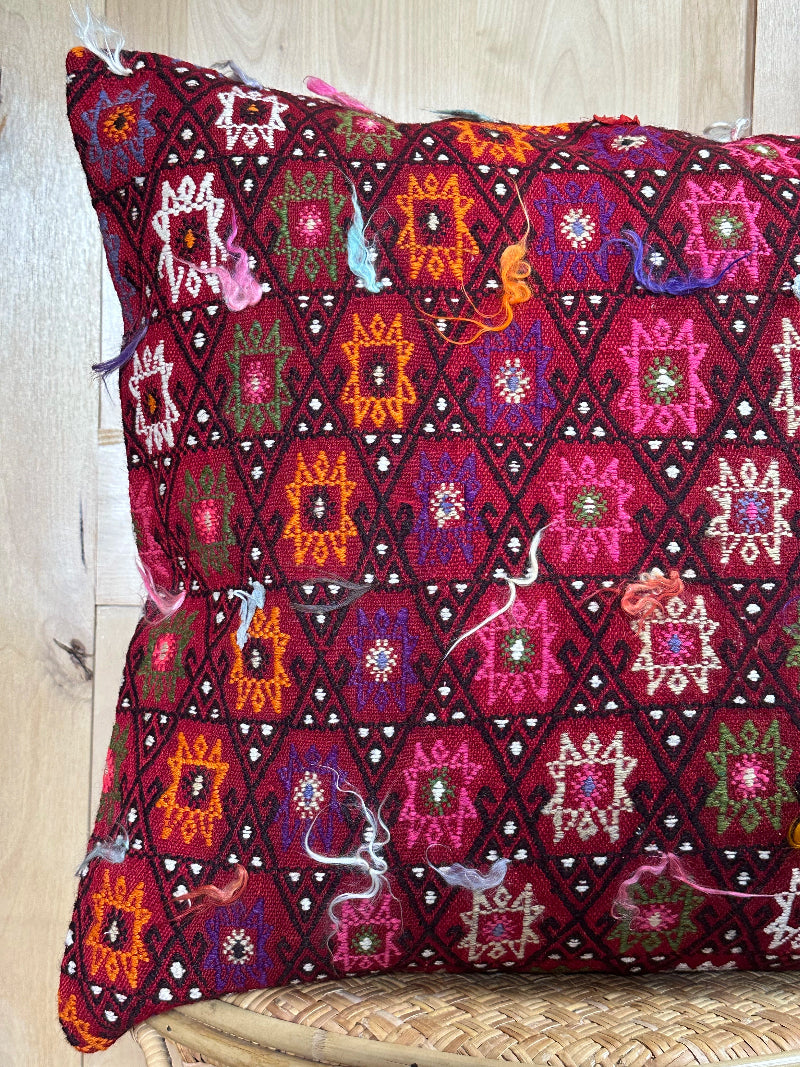 Bold handcrafted kilim pillow with intricate Berber-inspired embroidery. Made from repurposed vintage textiles in deep red, magenta, and orange hues with textured fringe details.