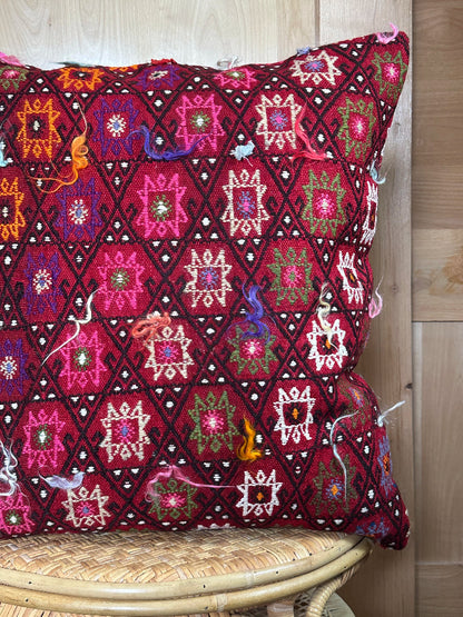 Bold handcrafted kilim pillow with intricate Berber-inspired embroidery. Made from repurposed vintage textiles in deep red, magenta, and orange hues with textured fringe details.
