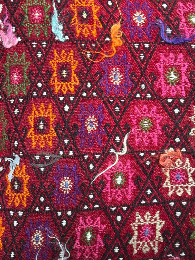 Bold handcrafted kilim pillow with intricate Berber-inspired embroidery. Made from repurposed vintage textiles in deep red, magenta, and orange hues with textured fringe details.