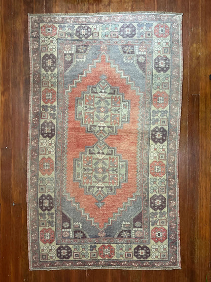 Vintage Turkish handwoven wool rug featuring a double medallion design in muted red, blue, and sage green tones with a detailed floral border.