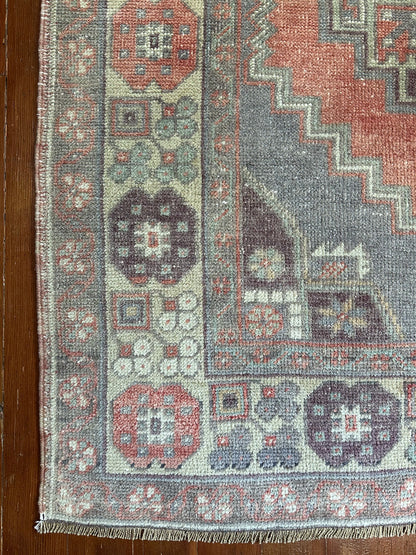 Vintage Turkish handwoven wool rug featuring a double medallion design in muted red, blue, and sage green tones with a detailed floral border.
