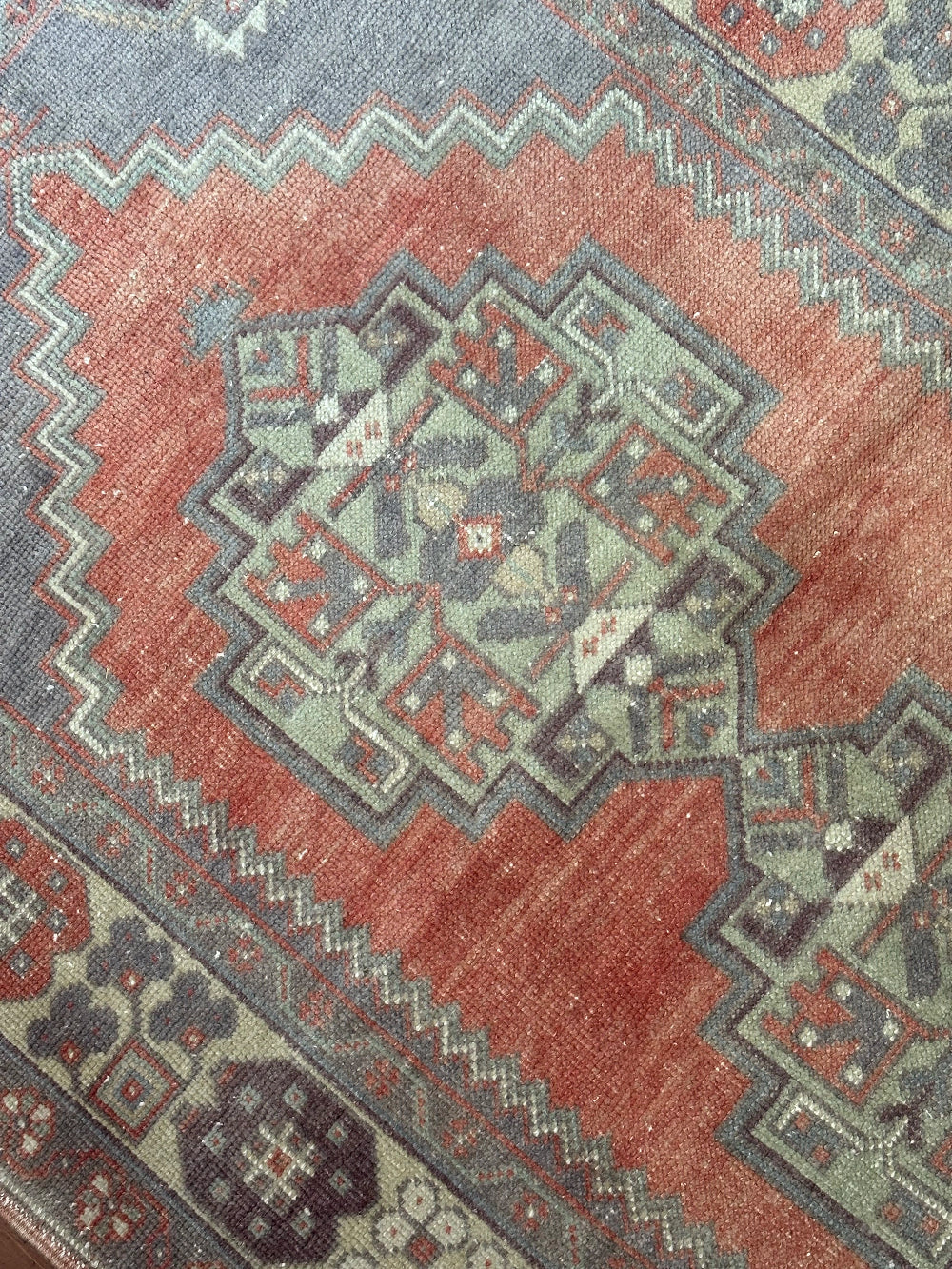 Vintage Turkish handwoven wool rug featuring a double medallion design in muted red, blue, and sage green tones with a detailed floral border.