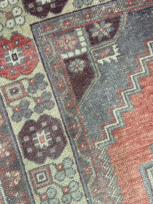 Vintage Turkish handwoven wool rug featuring a double medallion design in muted red, blue, and sage green tones with a detailed floral border.
