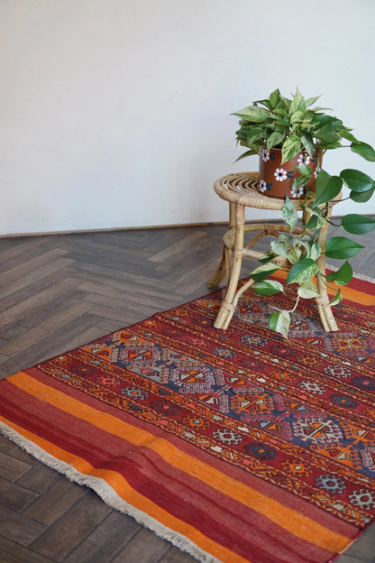 5 by 3 red and orange Turkish area rug featuring a striped pattern on the outside edges and a central striped pattern with geometric shapes and embroidery