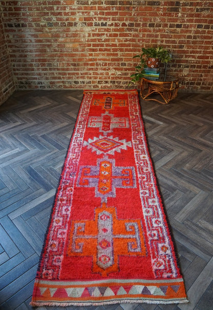 11 foot by 3 foot Herki Turkish runner with beautiful deep red pile as the main color, border on each side with triangles in orange, purple, light blue and cream and large medallions in the center