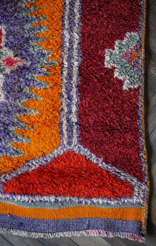 11.5 foot by 3 foot high pile Turkish Herki runner with long shaggy pile and a southwestern feel, orange, red and maroon base coloring and accents of purple, light blue and pink.