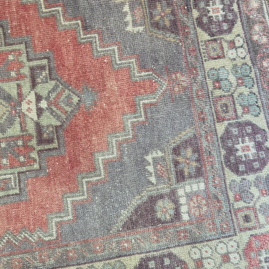 Vintage Turkish handwoven wool rug featuring a double medallion design in muted red, blue, and sage green tones with a detailed floral border.