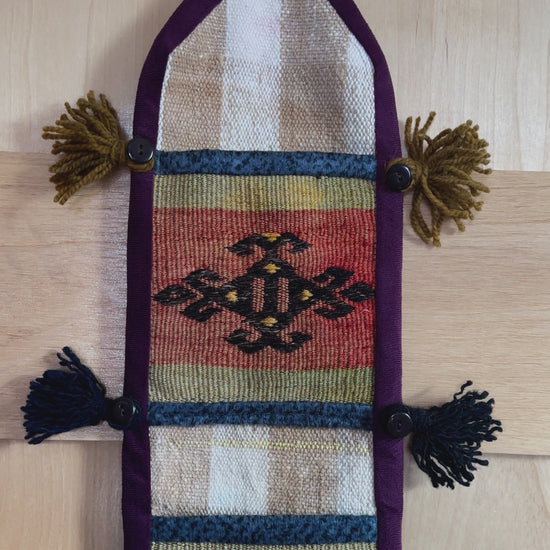 Handmade Turkish wall hanging with vintage rug patterns, featuring colorful tassels, evil eye beads, and geometric designs on a wood panel background. Unique bohemian decor made from authentic Turkish rug fragments, perfect for home styling.