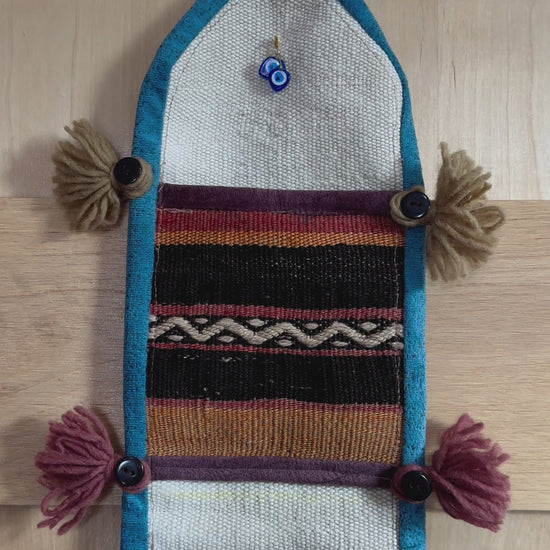 Handmade Turkish wall hanging with vintage rug patterns, featuring colorful tassels, evil eye beads, and geometric designs on a wood panel background. Unique bohemian decor made from authentic Turkish rug fragments, perfect for home styling.