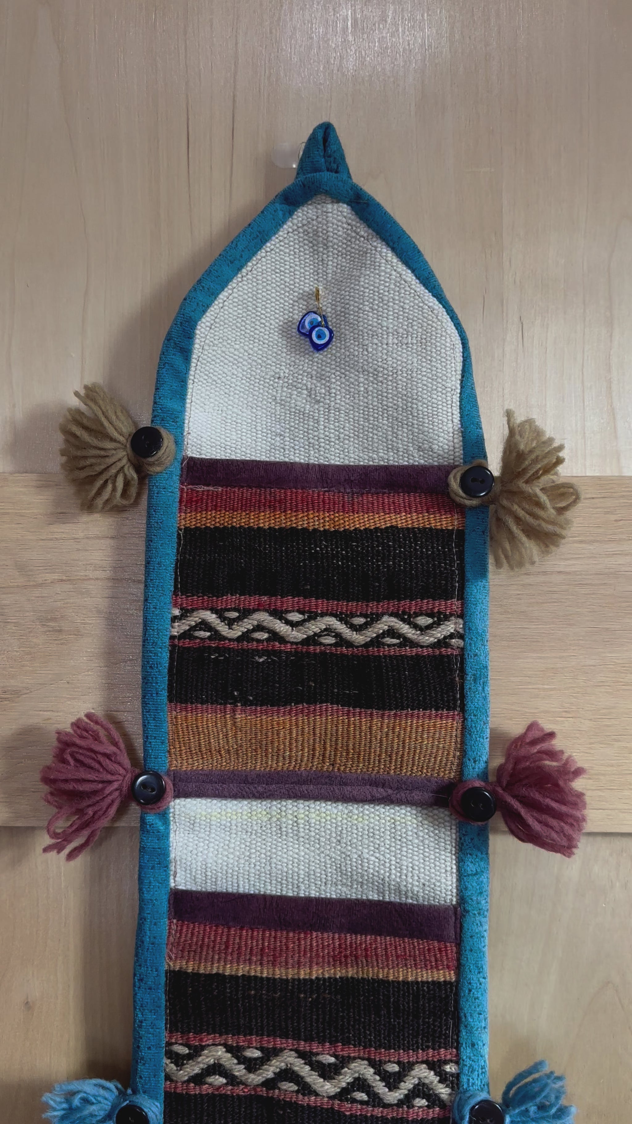 Handmade Turkish wall hanging with vintage rug patterns, featuring colorful tassels, evil eye beads, and geometric designs on a wood panel background. Unique bohemian decor made from authentic Turkish rug fragments, perfect for home styling.