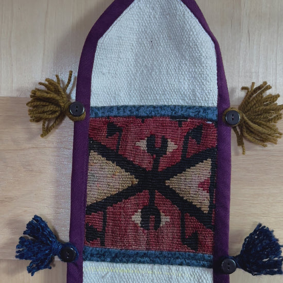 Handmade Turkish wall hanging with vintage rug patterns, featuring colorful tassels, evil eye beads, and geometric designs on a wood panel background. Unique bohemian decor made from authentic Turkish rug fragments, perfect for home styling.