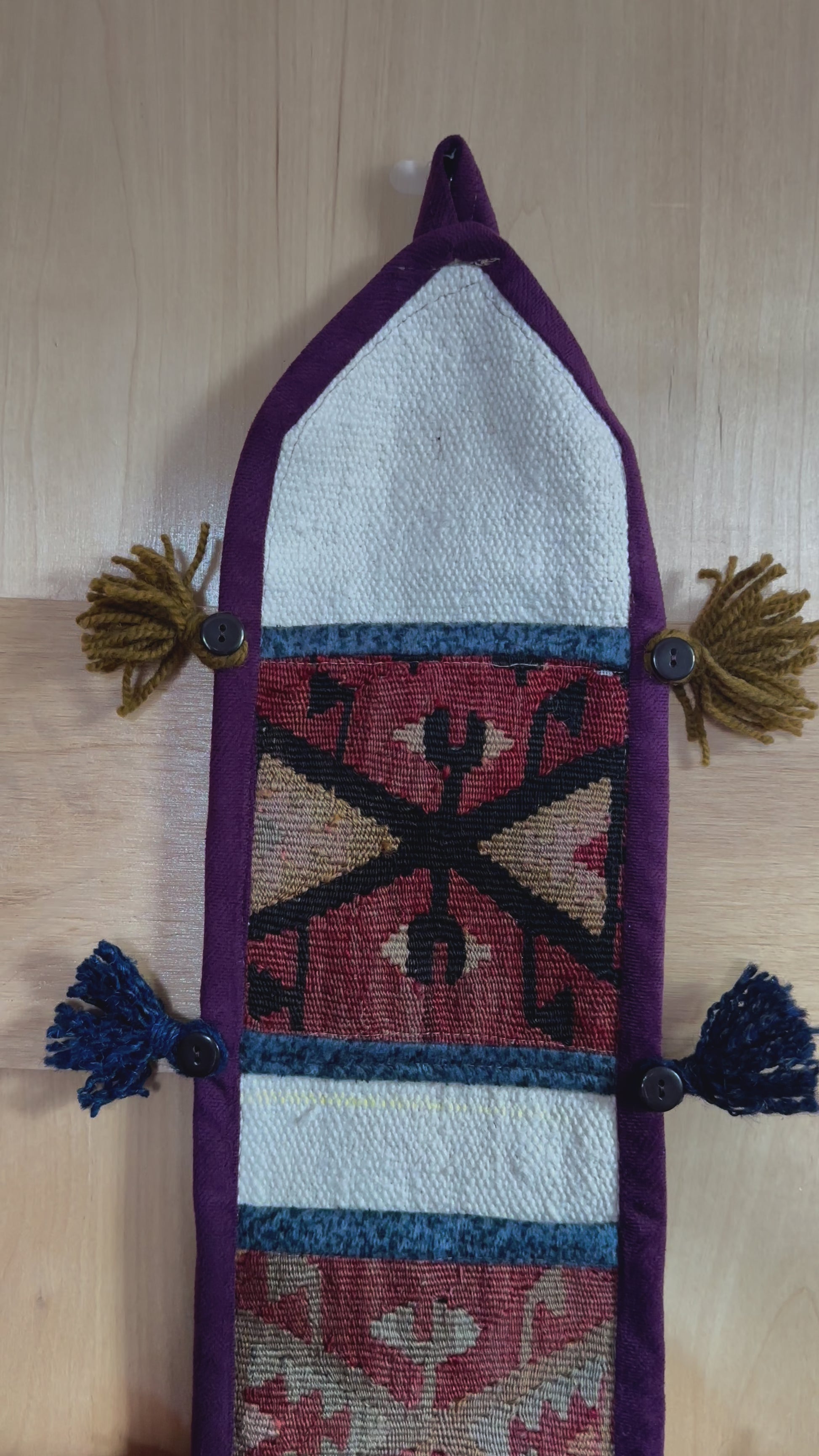 Handmade Turkish wall hanging with vintage rug patterns, featuring colorful tassels, evil eye beads, and geometric designs on a wood panel background. Unique bohemian decor made from authentic Turkish rug fragments, perfect for home styling.