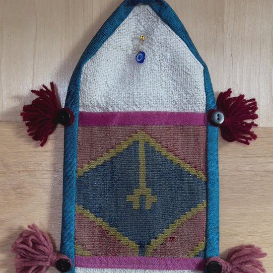 Handmade Turkish wall hanging with vintage rug patterns, featuring colorful tassels, evil eye beads, and geometric designs on a wood panel background. Unique bohemian decor made from authentic Turkish rug fragments, perfect for home styling.