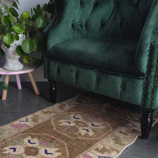 Handmade neutral Turkish mini rug featuring sand, brown and pops of pink and blue with geometric patterns around the border