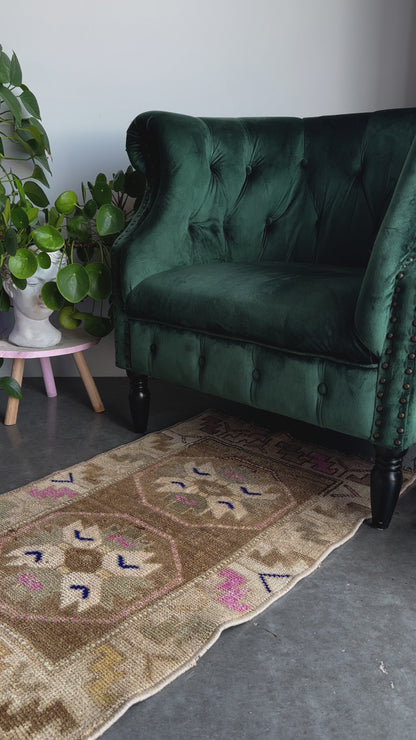 Handmade neutral Turkish mini rug featuring sand, brown and pops of pink and blue with geometric patterns around the border