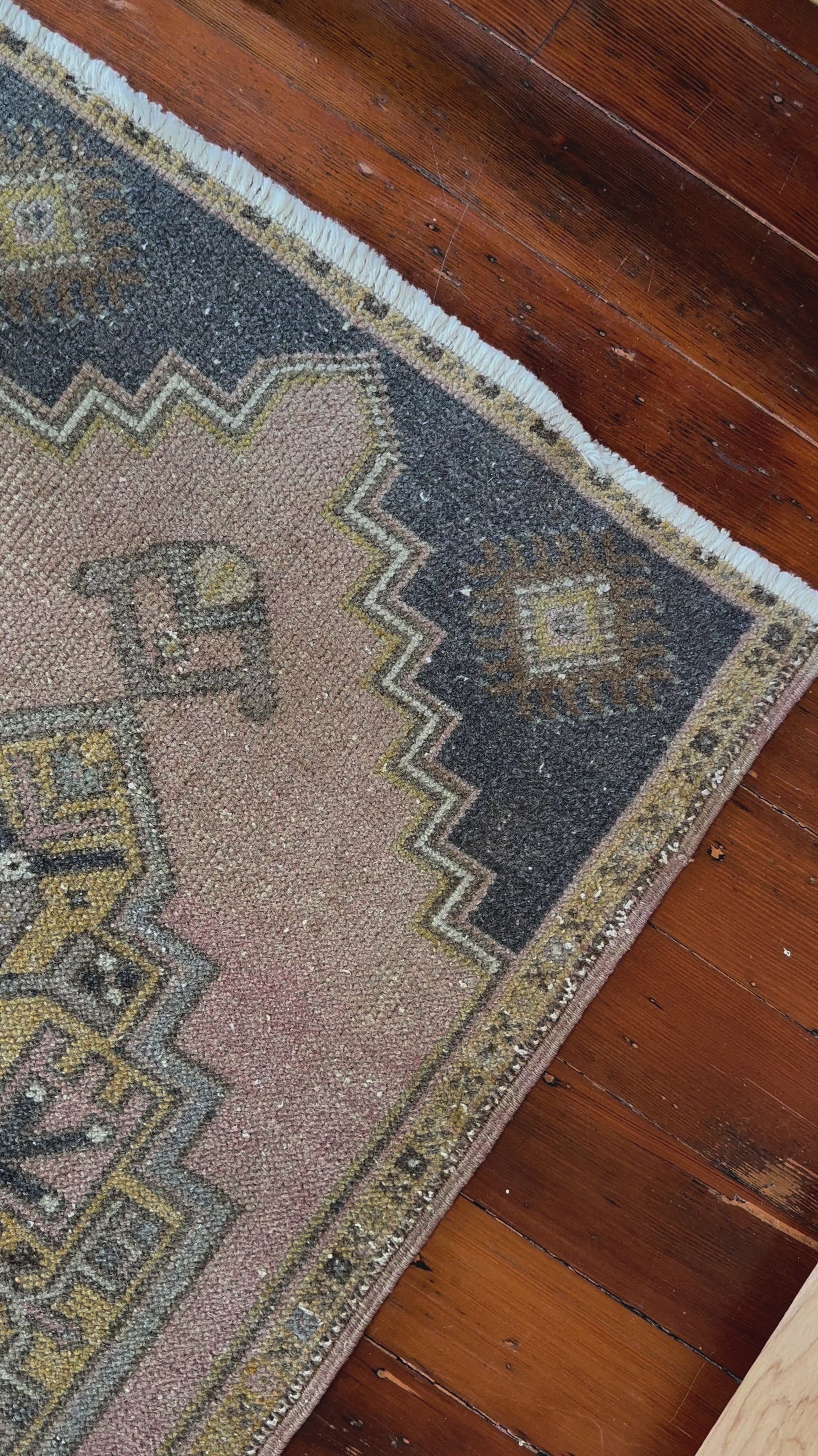 Vintage Turkish wool rug with a central geometric medallion in muted pink, gold, and dark charcoal tones, featuring stepped corner motifs and a distressed finish.