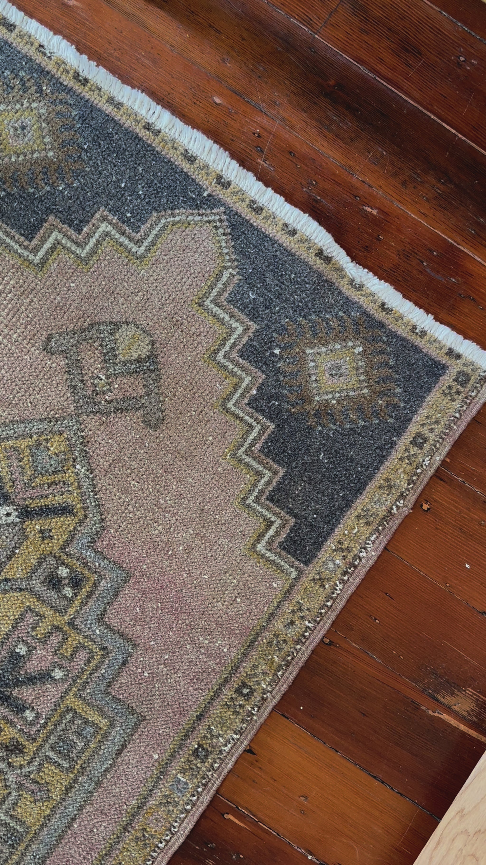 Vintage Turkish wool rug with a central geometric medallion in muted pink, gold, and dark charcoal tones, featuring stepped corner motifs and a distressed finish.