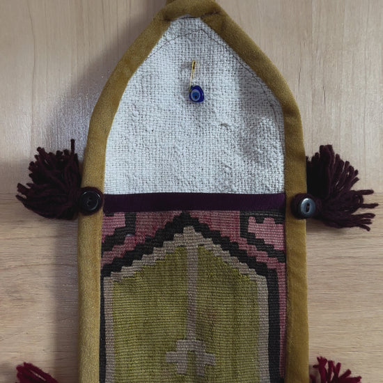 Handmade Turkish wall hanging with vintage rug patterns, featuring colorful tassels, evil eye beads, and geometric designs on a wood panel background. Unique bohemian decor made from authentic Turkish rug fragments, perfect for home styling.