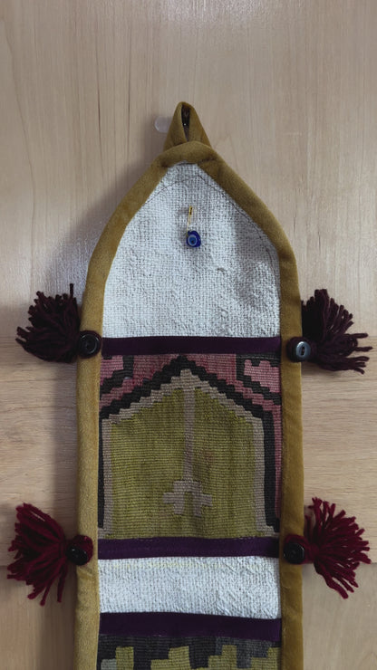 Handmade Turkish wall hanging with vintage rug patterns, featuring colorful tassels, evil eye beads, and geometric designs on a wood panel background. Unique bohemian decor made from authentic Turkish rug fragments, perfect for home styling.