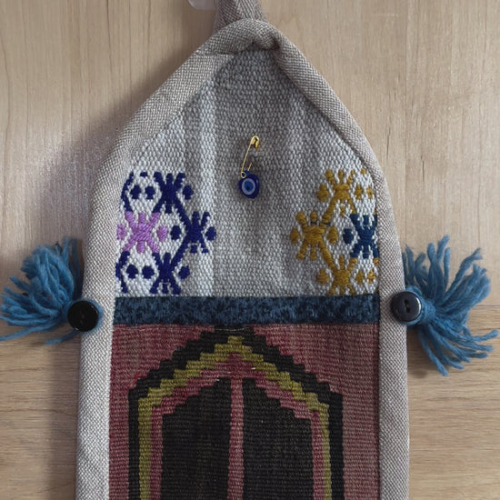 Handmade Turkish wall hanging with vintage rug patterns, featuring colorful tassels, evil eye beads, and geometric designs on a wood panel background. Unique bohemian decor made from authentic Turkish rug fragments, perfect for home styling.