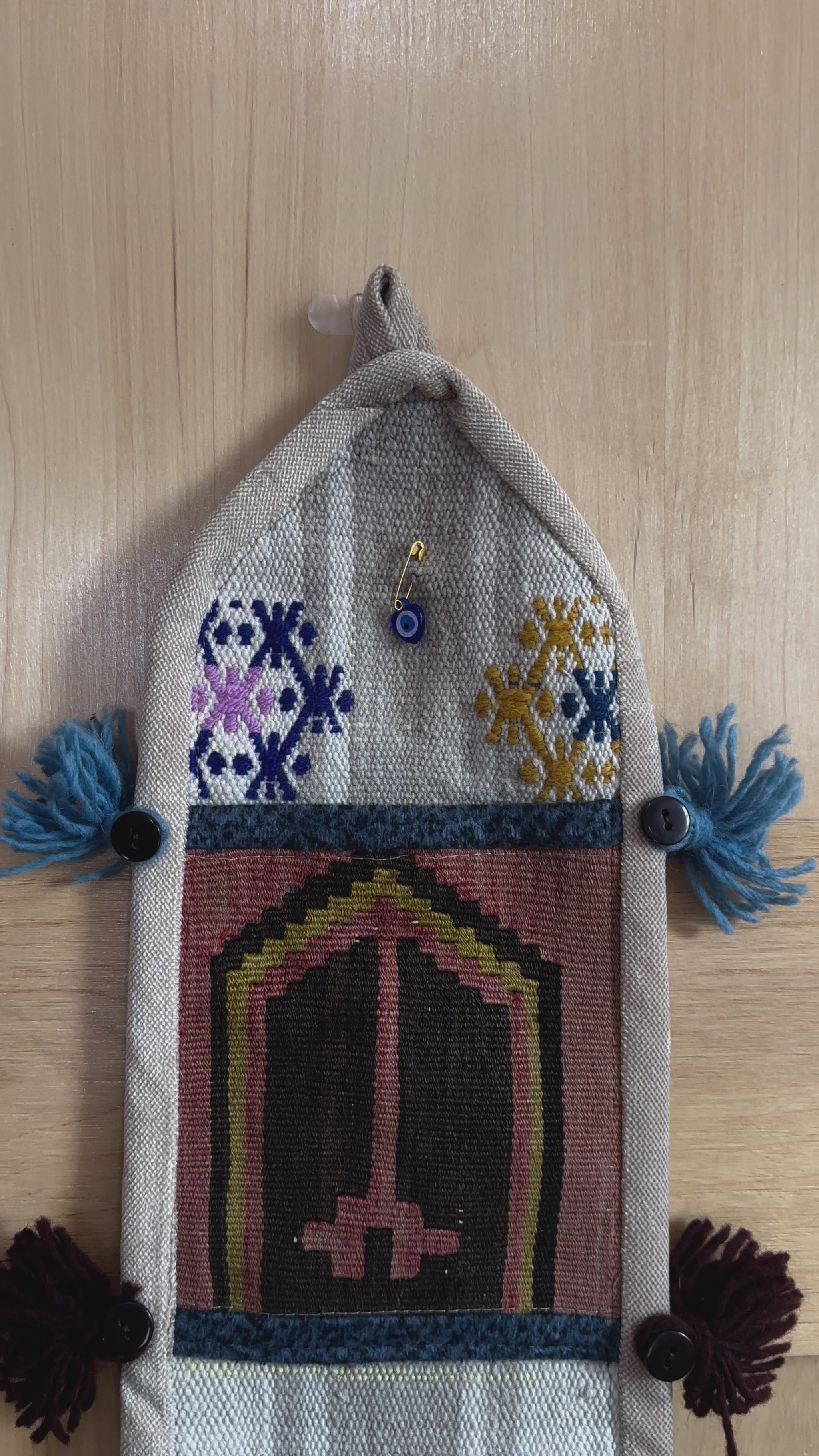 Handmade Turkish wall hanging with vintage rug patterns, featuring colorful tassels, evil eye beads, and geometric designs on a wood panel background. Unique bohemian decor made from authentic Turkish rug fragments, perfect for home styling.