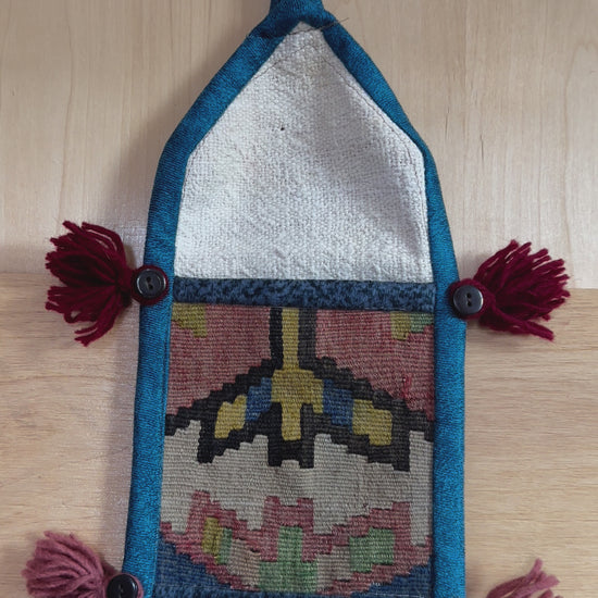 Handmade Turkish wall hanging with vintage rug patterns, featuring colorful tassels, evil eye beads, and geometric designs on a wood panel background. Unique bohemian decor made from authentic Turkish rug fragments, perfect for home styling.