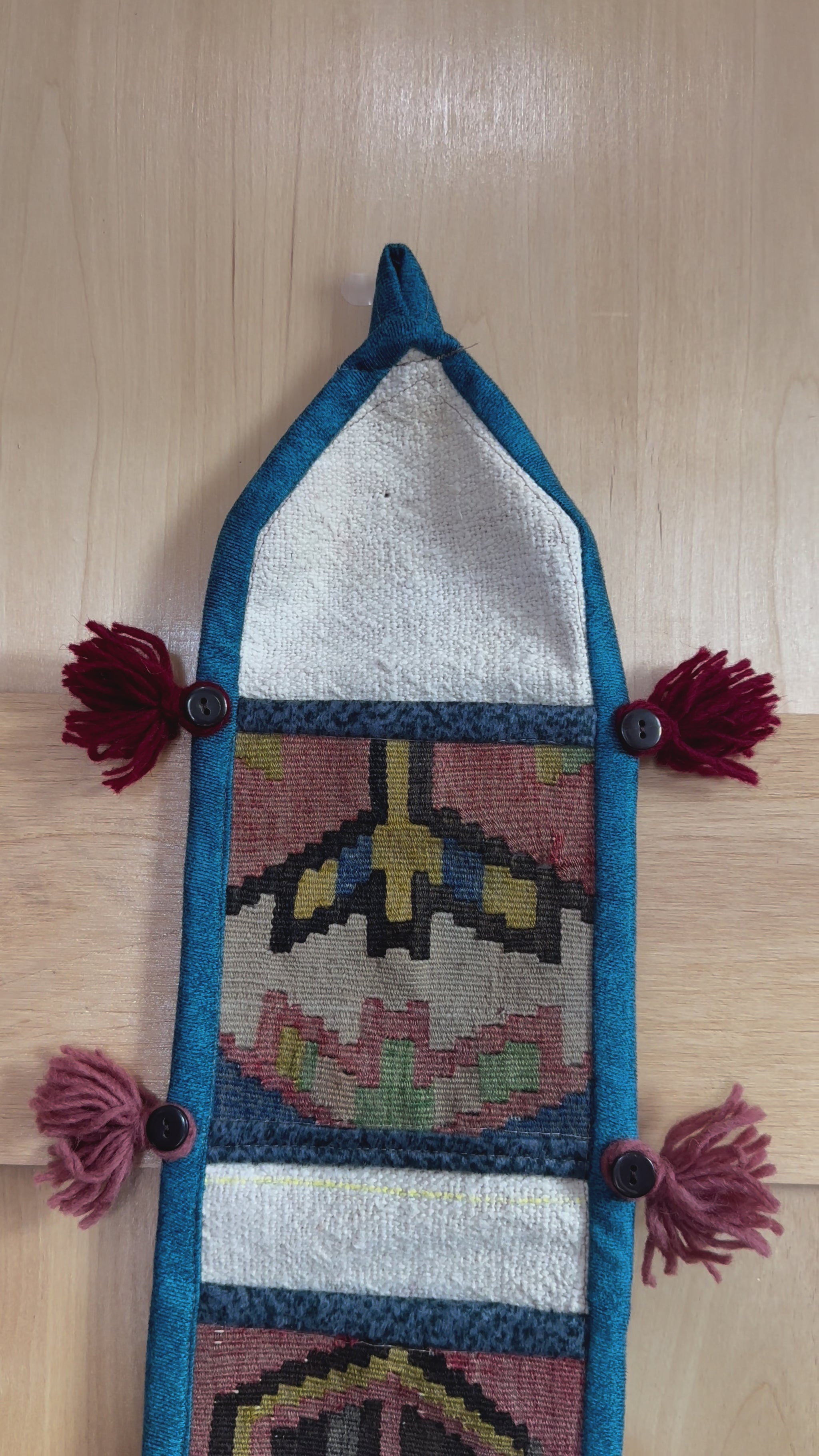 Handmade Turkish wall hanging with vintage rug patterns, featuring colorful tassels, evil eye beads, and geometric designs on a wood panel background. Unique bohemian decor made from authentic Turkish rug fragments, perfect for home styling.