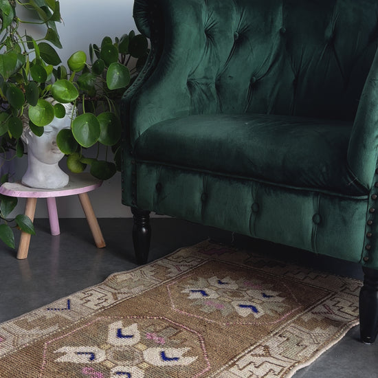 Handmade neutral Turkish mini rug featuring sand, brown and pops of pink and blue with geometric patterns around the border