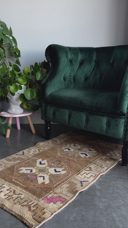 Handmade neutral Turkish mini rug featuring sand, brown and pops of pink and blue with geometric patterns around the border